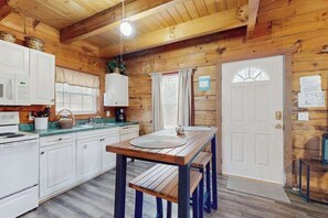 A wooden cabin-style kitchen with white cabinets, a wooden table, and a white door.