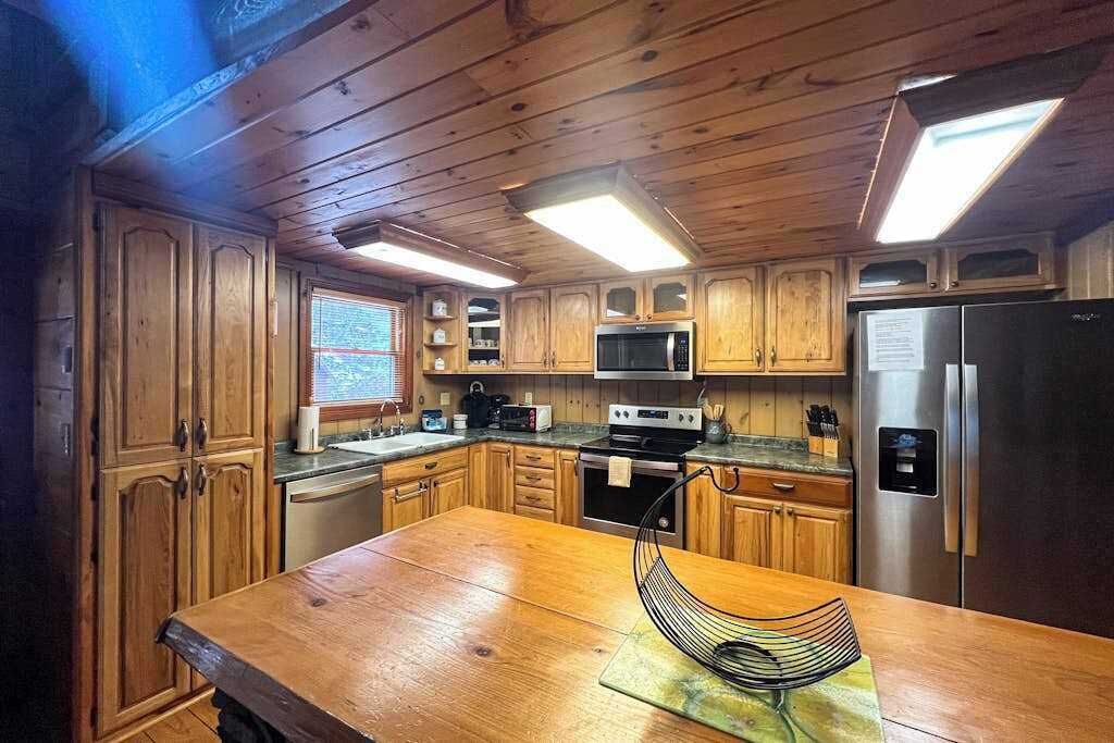 Une cuisine de style rustique, avec des meubles en bois intégrés, un îlot central, un four à micro-ondes, une cuisinière et un réfrigérateur.