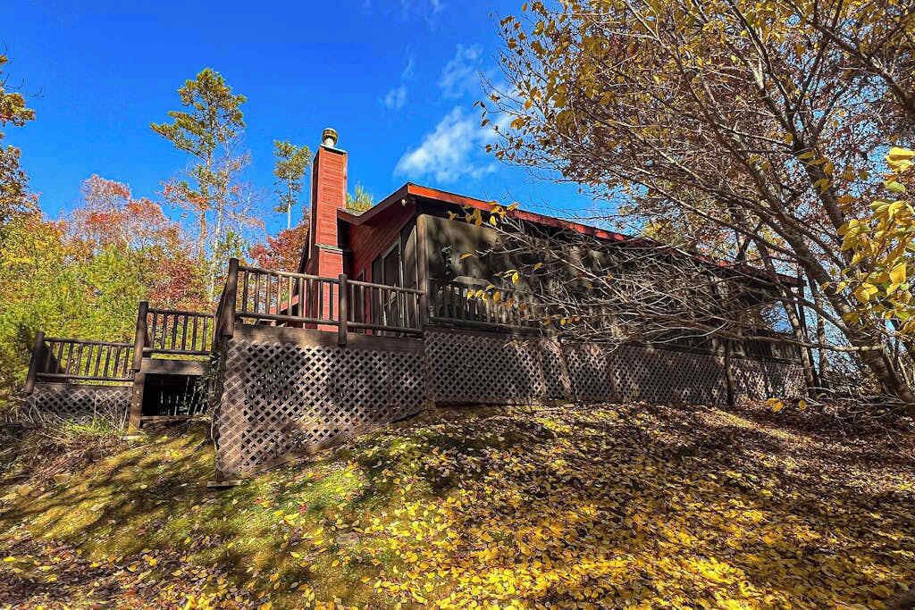 Un chalet rustique doté d’une cheminée, entouré d’arbres et agrémenté d’une terrasse en bois.