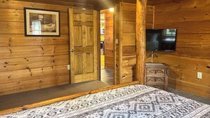 A wooden cabin room with a bed, a television, a dresser, and a door leading to another room. - Best Kept Secret Stay (Blue Ridge)