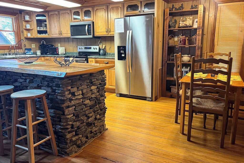 Eine Küche mit Holzausstattung, einem Edelstahl-Kühlschrank, einer Wand mit Steinverkleidung und einem Essbereich mit Holzsesseln.