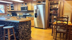 A kitchen with wooden cabinets, a stainless steel refrigerator, a stone accent wall, and a dining area with wooden chairs. - Best Kept Secret Stay (Blue Ridge)