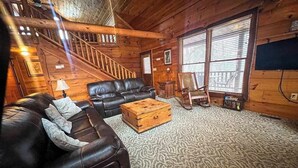 A log cabin interior with a staircase, leather sofa, wooden chest, and large windows. - Best Kept Secret Stay (Blue Ridge)