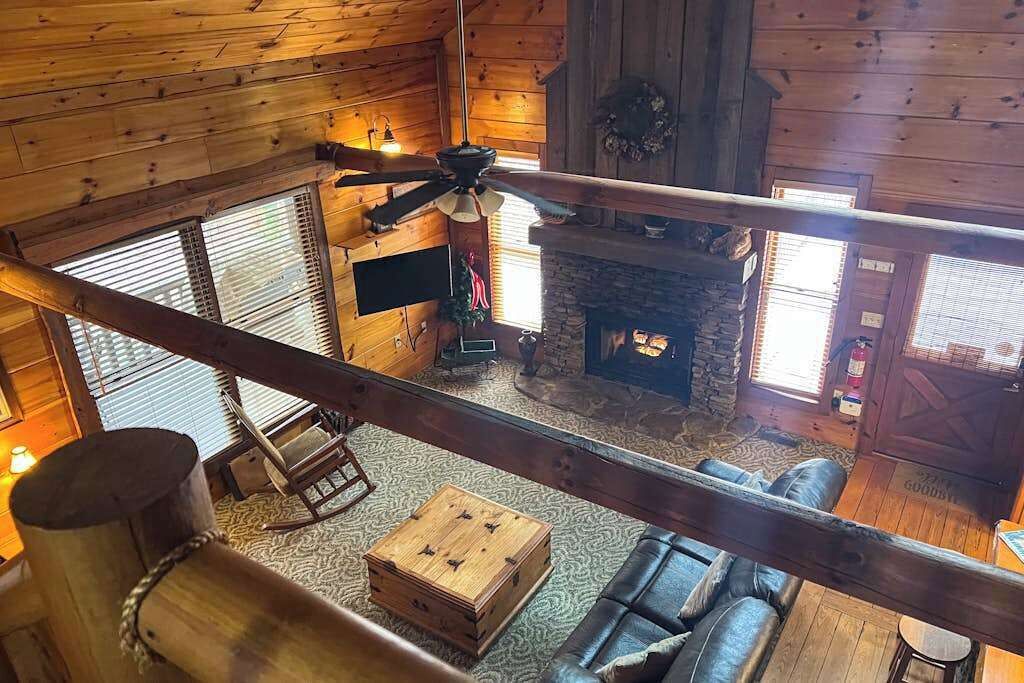 L’intérieur d’une cabane est agrémenté d’une cheminée en pierre, de murs en bois, d’un ventilateur de plafond et d’un coin salon confortable.