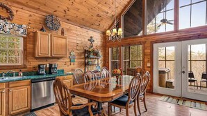 Un interior de madera con una mesa de comedor, sillas, una zona de cocina y ventanas amplias.