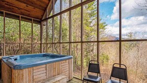 Una bañera de hidromasaje de madera con dos sillas en una terraza con ventanales grandes.