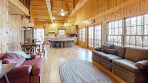 A spacious cabin interior with a dining area, kitchen, and a large window providing natural light. - Osprey Landing Retreat (Clarkesville)