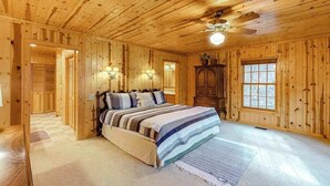 A wooden-paneled bedroom with a bed, two wall sconces, a ceiling fan, and a window. - Osprey Landing Retreat (Clarkesville)