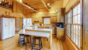 A wooden cabin-style kitchen with a central island, bar stools, and large windows. - Osprey Landing Retreat (Clarkesville)