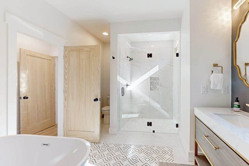 A modern bathroom with a glass-enclosed shower, a white bathtub, and a vanity with a mirror.