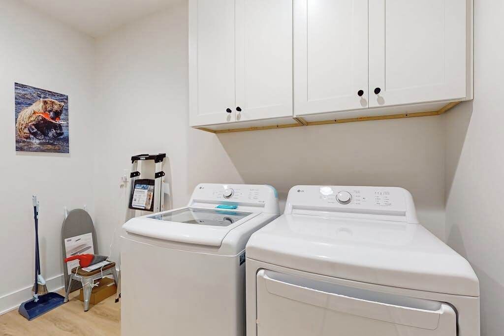 A laundry room with two white front-loading washing machines, a small table with a red object, a mop, and a wall-mounted laundry scale.