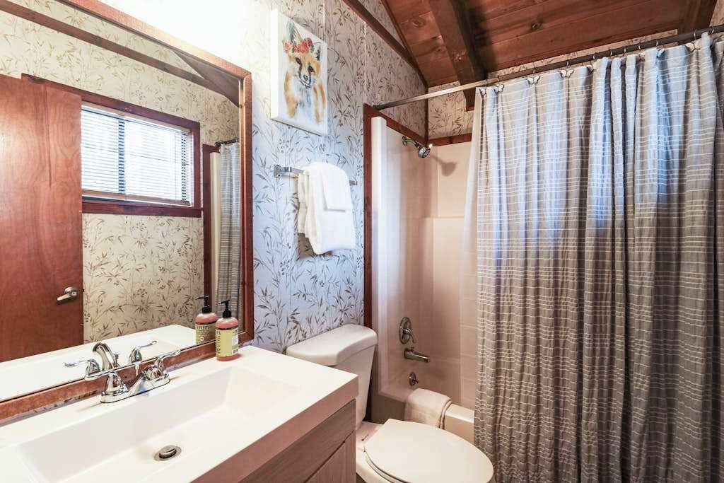 A bathroom with a sink, mirror, toilet, shower curtain, and a towel rack.