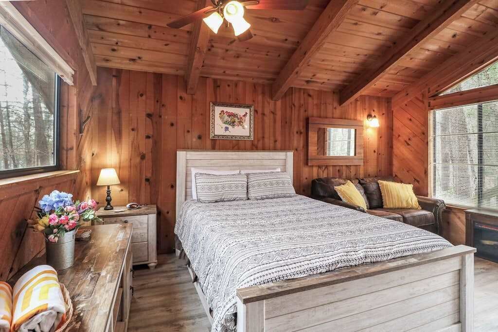 A wooden cabin bedroom with a bed, a nightstand, a lamp, a dresser, and a window.