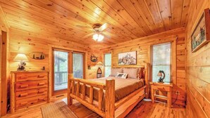 A log cabin bedroom with a wooden bed, a dresser, a nightstand, and a ceiling fan. - Red Oak Luxe Mountain Cabin (Blue Ridge)