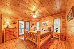 A log cabin bedroom with a wooden bed, a dresser, a nightstand, and a ceiling fan. - Red Oak Luxe Mountain Cabin (Blue Ridge)
