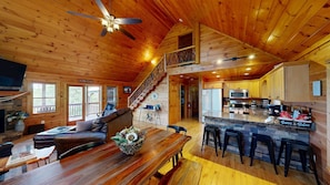 A cabin interior with a wooden ceiling, a dining area, a kitchen with a stone countertop, and a staircase leading to an upper level. - Red Oak Luxe Mountain Cabin (Blue Ridge)