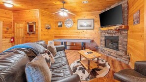 A log cabin interior with a leather sofa, a pool table, a fireplace, and a mounted TV. - Red Oak Luxe Mountain Cabin (Blue Ridge)