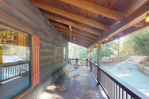 A covered porch with wooden beams, a bench, and a view of a forested area. - Lazy Bear Cabin Sautee (Ellijay)