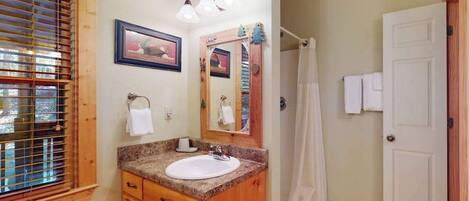 A bathroom with a wooden vanity, a sink, a mirror, and a shower curtain.
