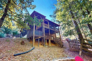 Une cabane en bois dotée d’un balcon, entourée d’arbres et d’une clôture en bois.
