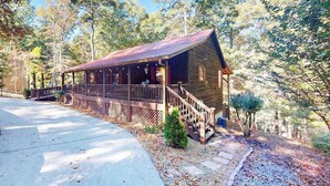 Eine rustikale Holzhütte mit Veranda, umgeben von Bäumen und einem Betonweg.