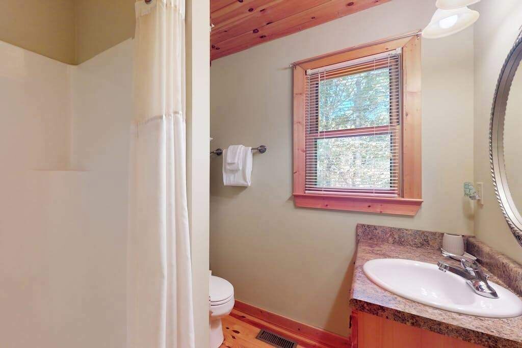 Un baño con techo de madera, una ventana con persianas, un inodoro blanco y una encimera de granito con un lavamanos.