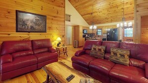 Ein Blockhaus-Interieur mit Holzwänden und -decke, einer Küchenzeile und zwei Ledersofas mit Kissen.