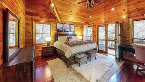 Une chambre à coucher située dans une cabane en rondins, avec un lit, deux tables de chevet, un bureau, une chaise et un ventilateur de plafond.