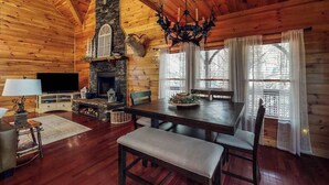L’intérieur d’une cabane en rondins, avec une cheminée en pierre, un plafond en bois et un téléviseur.
