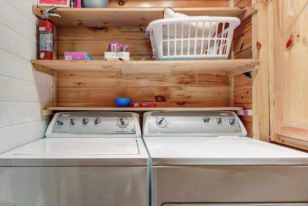 Een wasruimte met twee voorladers, een houten plank met een wasmand, en een brandblusser.