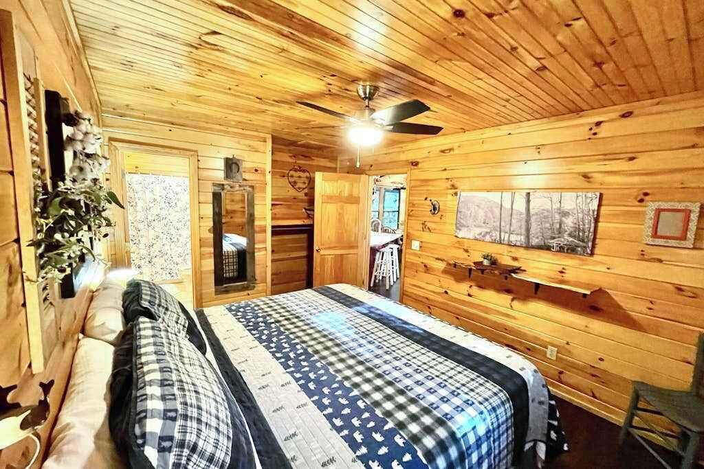 Dormitorio de cabaña de madera con cama, ventilador de techo, ventana y estante fijado a la pared.