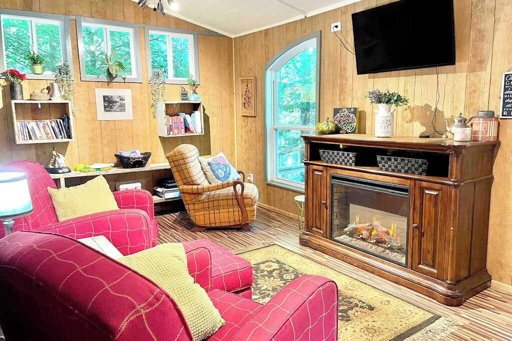 A cozy living room with a fireplace, red sofas, a plaid armchair, and wooden walls.