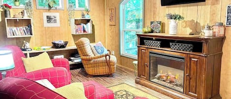 A cozy living room with a fireplace, red sofas, a plaid armchair, and wooden walls.