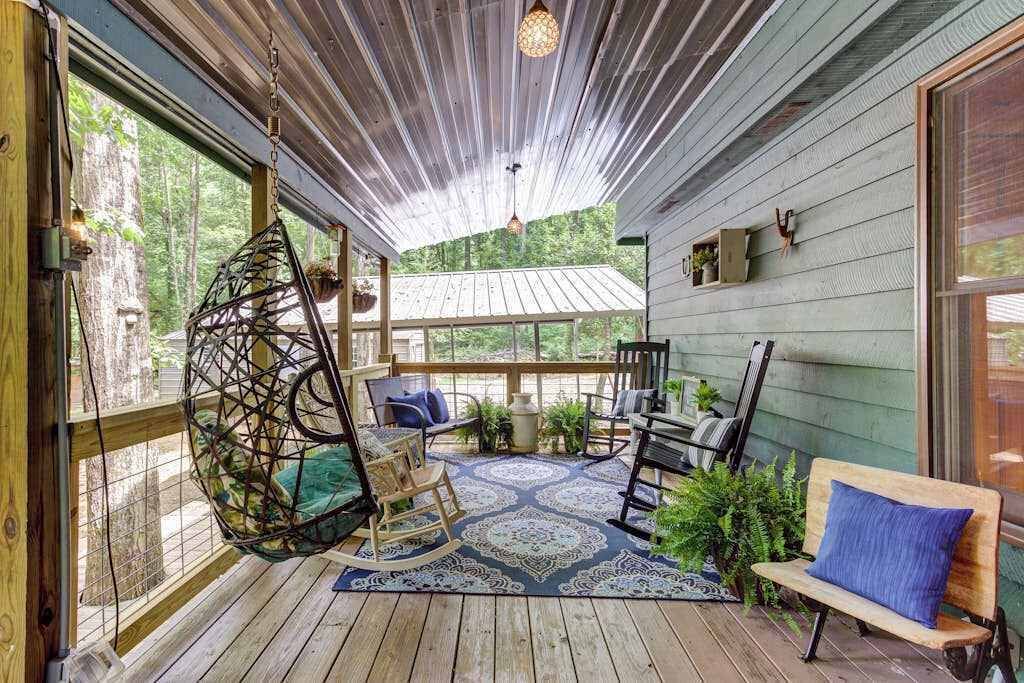 A covered porch with a hanging chair, a bench, and a table with chairs.