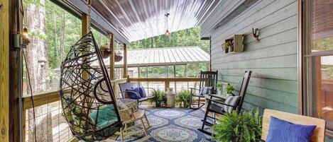 A covered porch with a hanging chair, a bench, and a table with chairs.