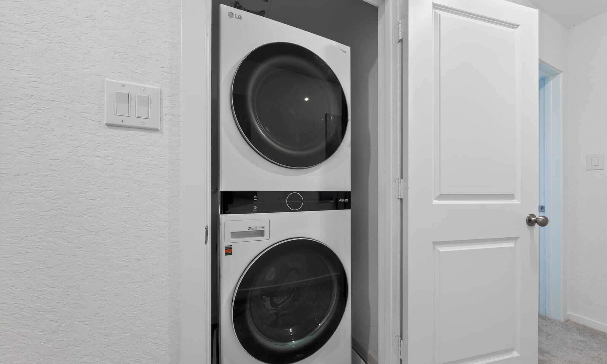 Uma lavanderia com duas máquinas de lavar e secar empilhadas, uma porta branca e um interruptor de luz na parede.