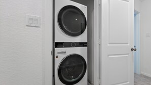 Una sala de lavandería con dos lavadoras y secadoras apiladas, una puerta blanca y un interruptor de luz en la pared.