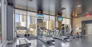 A gym with treadmills, exercise bikes, and a pool view. - Designer 1BR at Beachwalk - Pool & Beach (Hallandale Beach)