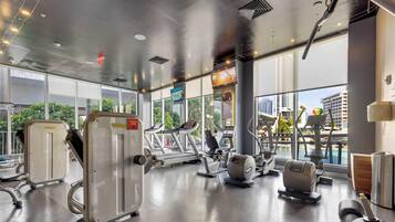 A gym with cardio machines, weight stations, and a large window with a city view.