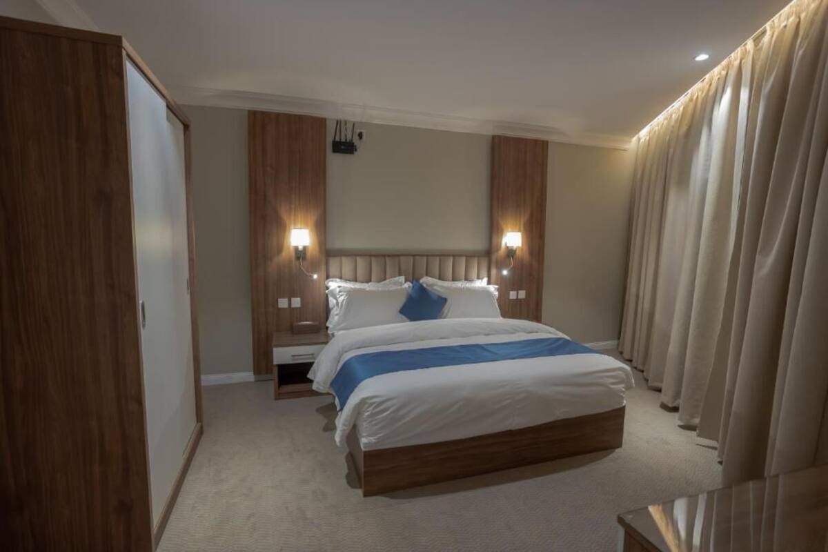 A hotel room with a large bed, wooden headboard, two bedside lamps, and a view of the cityscape.