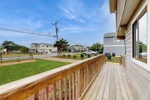 A wooden deck with a railing, a grassy lawn, and houses in the background. - Sandbridge Gem with Sunroom, Private Pool & Yard (Virginia Beach)