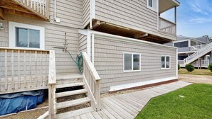 Un bâtiment à deux étages doté d’une terrasse en bois, d’un espace extérieur couvert et d’un petit jardin.