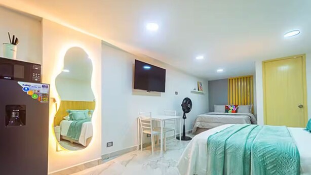 Ein Hotelzimmer mit Bett, Schreibtisch, Stuhl, Fernseher, Ventilator, Spiegel und einer Tür.