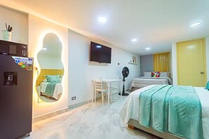 Hotelkamer met een bed, bureau, stoel, televisie, ventilator, spiegel en een deur.
