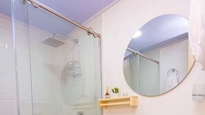 Ein Badezimmer mit Duschkabine aus Glas, Toilette, Waschbecken auf Säule und rundem Spiegel.