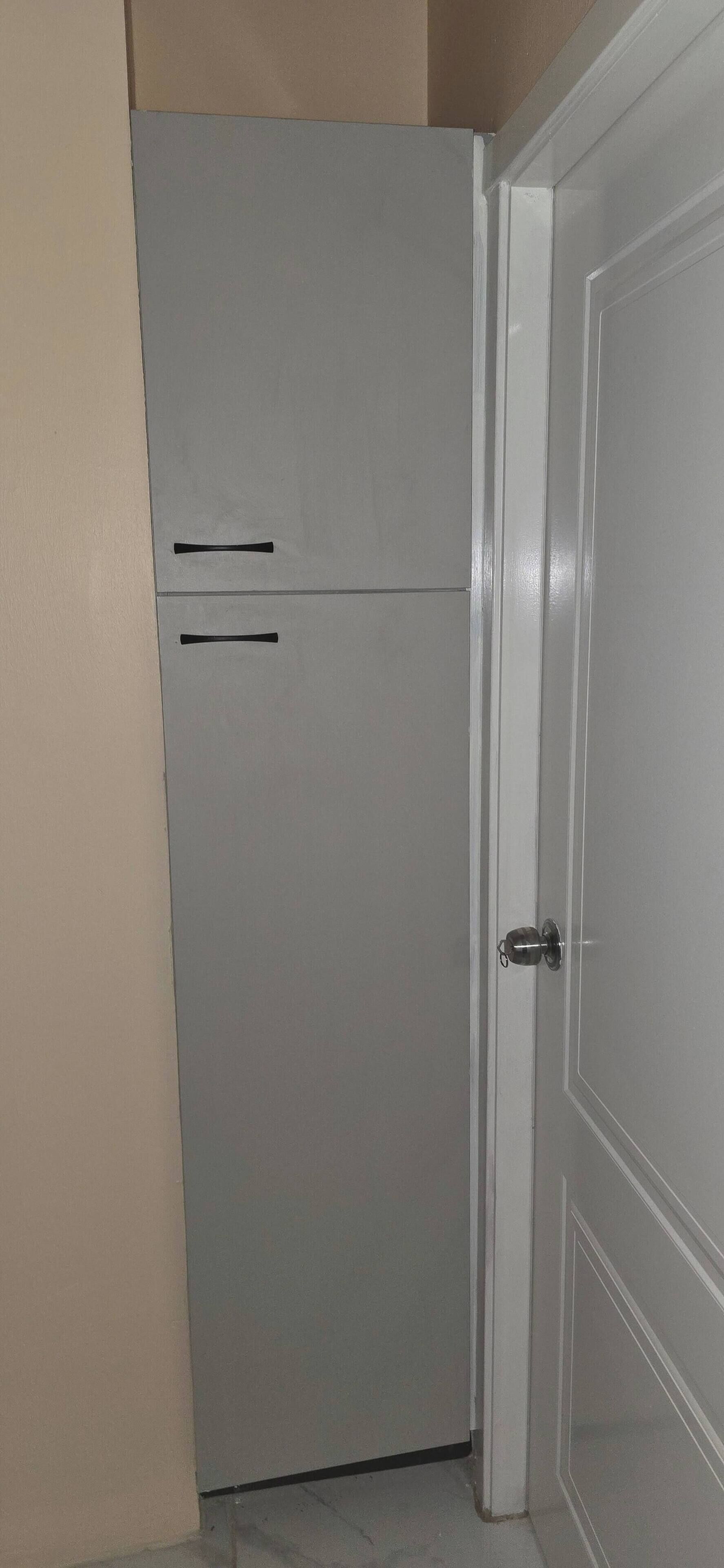 A white door with a silver handle, a white wall, and a grey cabinet with two handles.