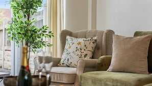 Ein Wohnzimmer mit einer Couch, einem kleinen Tisch mit Flasche und Gläsern sowie einer Topfpflanze.