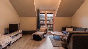 A modern living room with a TV, seating, and a view through a large window. - Alpine Apartment with Parking and Balcony (Hol)