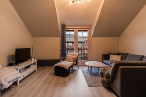 Un salon moderne avec un téléviseur, des sièges et une vue dégagée sur l’extérieur grâce à une grande fenêtre.