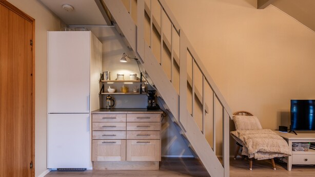 A kitchen with a refrigerator, wooden cabinets, a coffee maker, and a television in a living area with a staircase. - Alpine Apartment with Parking and Balcony (Hol)